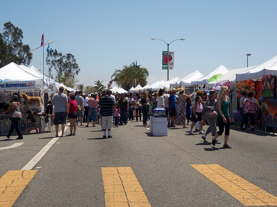 Festival-goers browsing rows of white art and craft booths on a sunny day