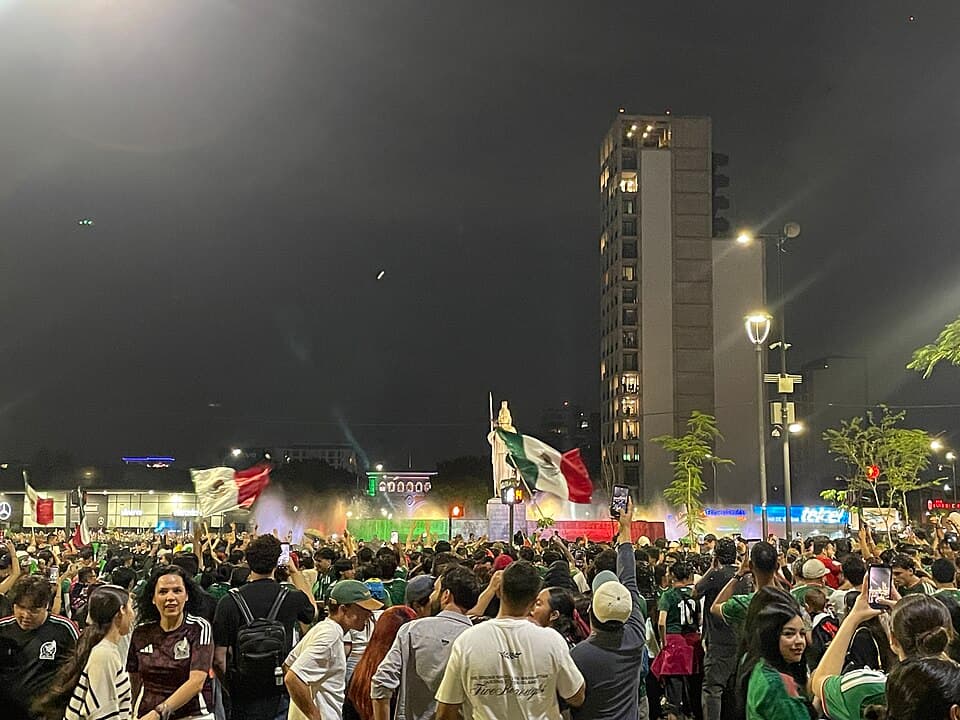 A huge nighttime crowd of soccer fans waving flags during the 2026 World Cup
